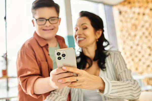 Foco no smartphone moderno em mãos de mãe alegre borrada e seu filho inclusivo com síndrome de Down — Fotografia de Stock