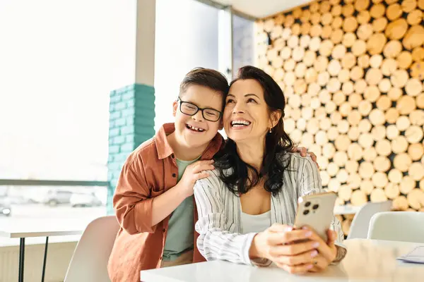 Menino alegre com síndrome de Down passar tempo com sua bela mãe no café, segurando smartphone — Fotografia de Stock