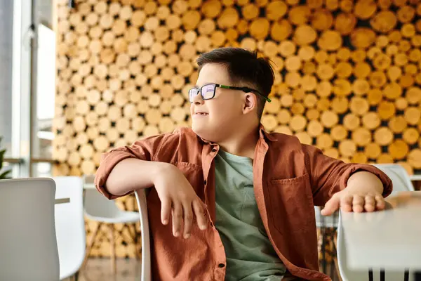 Alegre preadolescente inclusivo chico con síndrome de Down en traje casual mirando hacia otro lado mientras en la cafetería - foto de stock
