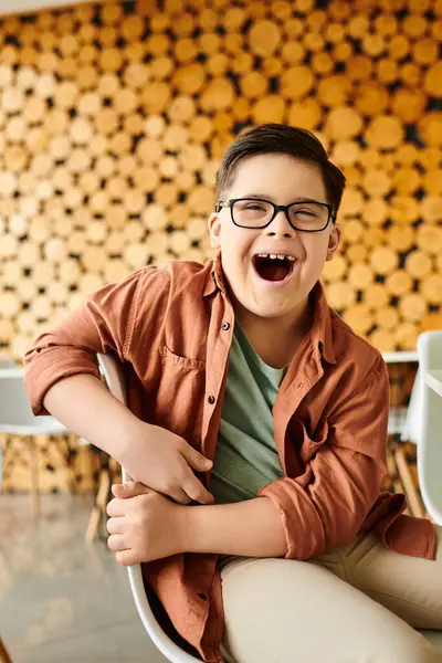 Happy inclusive preteen boy with Down syndrome with glasses sitting in cafe and laughing at camera — Stock Photo
