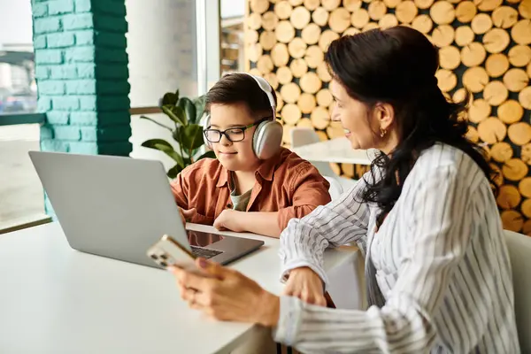 Cheerful mother spending time with her son with Down syndrome in cafe while he playing on laptop — Stock Photo