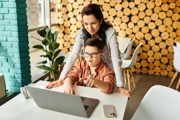Beautiful jolly mother looking at laptop with her inclusive cute son with Down syndrome in cafe — Stock Photo