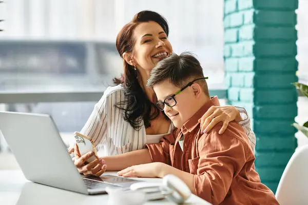 Очаровательный инклюзивный мальчик с синдромом Дауна проводит время со своей веселой матерью перед ноутбуком — стоковое фото