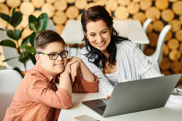 Adorable inclusive boy with Down syndrome spending time with his jolly mother in front of laptop — Stock Photo
