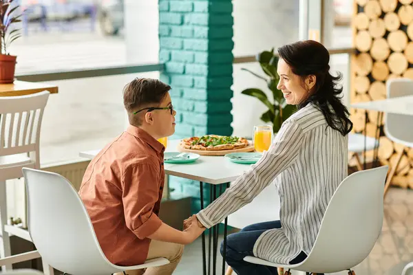 Beautiful mother eating pizza and drinking juice with her inclusive cute son with Down syndrome — Stock Photo