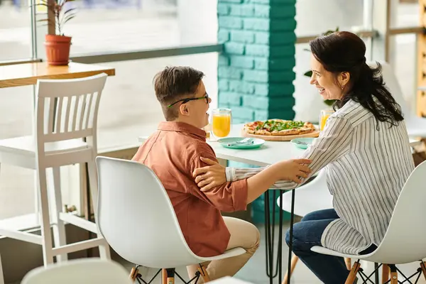 Belle mère manger de la pizza et boire du jus avec son fils mignon inclusif avec trisomie 21 — Photo de stock