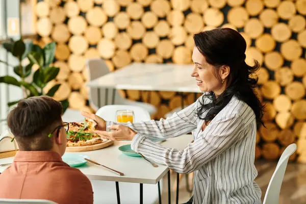 Beautiful mother eating pizza and drinking juice with her inclusive cute son with Down syndrome — Stock Photo