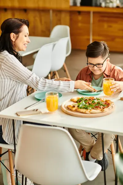 Приваблива мати їсть піцу і п'є сік зі своїм симпатичним сином з синдромом Дауна — стокове фото
