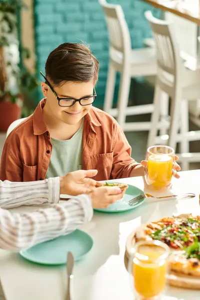 Good looking mother eating pizza and drinking juice with her inclusive cute son with Down syndrome — Stock Photo