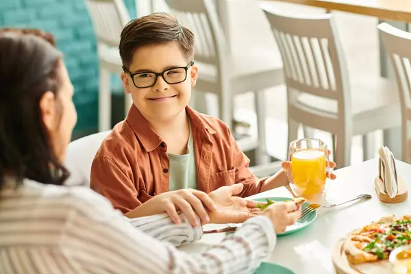 Gut aussehende Mutter isst Pizza und trinkt Saft mit ihrem netten Sohn mit Down-Syndrom — Stockfoto