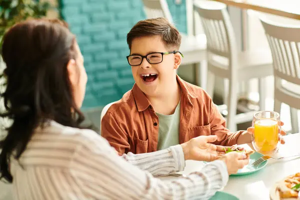 Cheerful mother eating pizza and drinking juice with her inclusive cute son with Down syndrome — Stock Photo