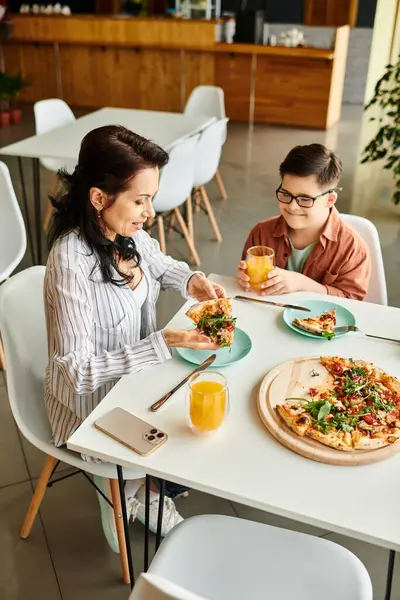 Щаслива мати їсть піцу і п'є сік зі своїм інклюзивним милим сином з синдромом Дауна — стокове фото