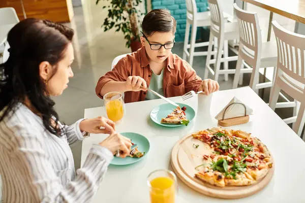Freudige Mutter, die mit ihrem netten Sohn mit Down-Syndrom Pizza isst und Saft trinkt — Stockfoto