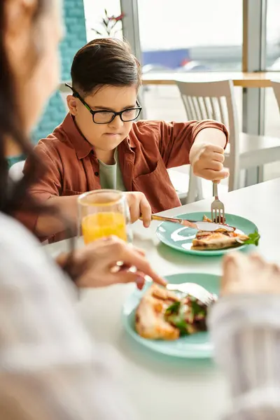 Joyful mother eating pizza and drinking juice with her inclusive cute son with Down syndrome — Stock Photo