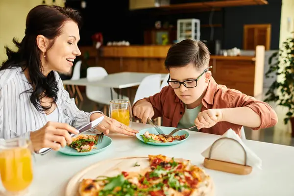 Joyful mother eating pizza and drinking juice with her inclusive cute son with Down syndrome — Stock Photo