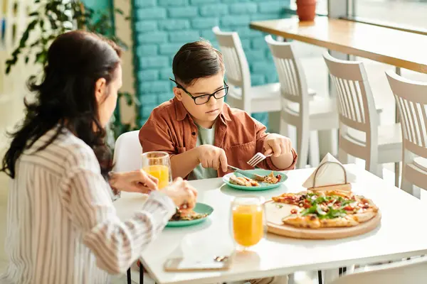 Положительная мать ест пиццу и пьет сок с ее включительно милый сын с синдромом Дауна — стоковое фото