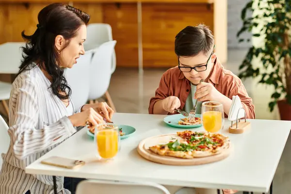 Fröhliche Mutter isst Pizza und trinkt Saft mit ihrem netten Sohn mit Down-Syndrom — Stockfoto