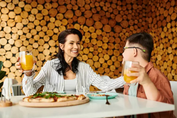 Happy mother eating pizza and drinking juice with her inclusive cute son with Down syndrome — Stock Photo