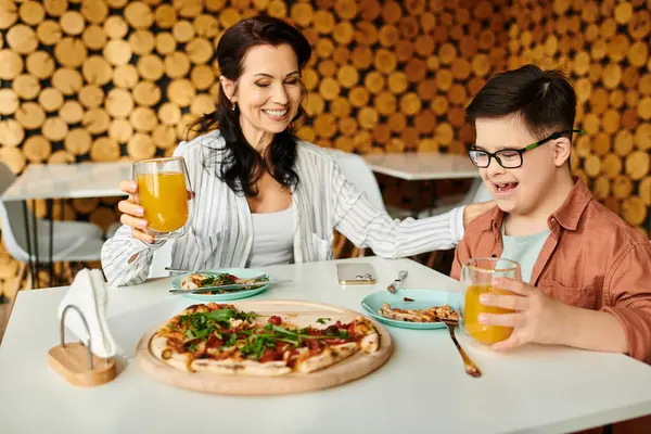Happy mother eating pizza and drinking juice with her inclusive cute son with Down syndrome — Stock Photo