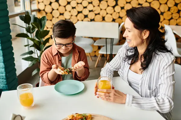 Feliz madre comer pizza y beber jugo con su hijo lindo inclusivo con síndrome de Down - foto de stock