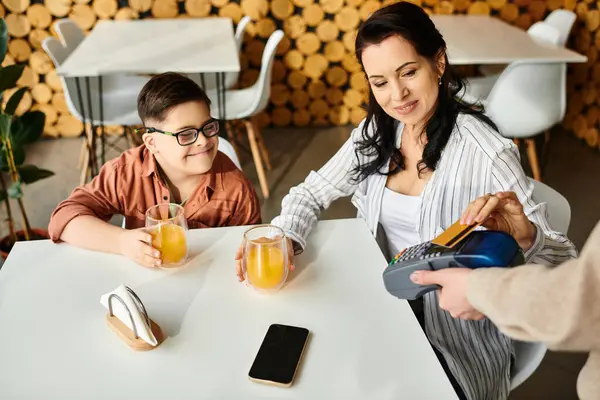 Красивая веселая мать платит кредитной картой рядом с ее включительно сын с синдромом Дауна в кафе — стоковое фото