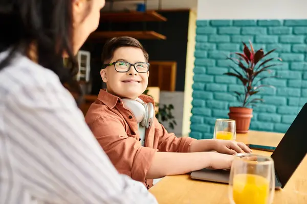 Joyous inclusive boy with Down syndrome with headphones playing on laptop near his mother in cafe — Stock Photo