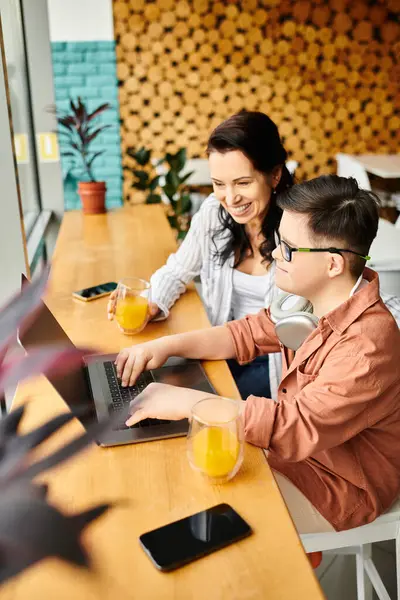 Joyful inclusive boy with Down syndrome with headphones playing on laptop near his mother in cafe — Stock Photo