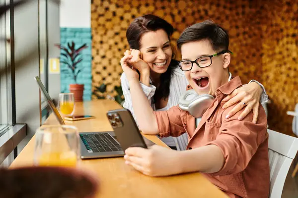 Веселий хлопчик з синдромом Дауна дивиться на смартфон біля своєї веселої матері в кафе — стокове фото
