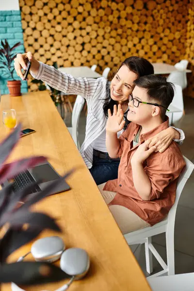 Beautiful joyous mother taking selfie with her preteen inclusive son with Down syndrome in cafe — Stock Photo