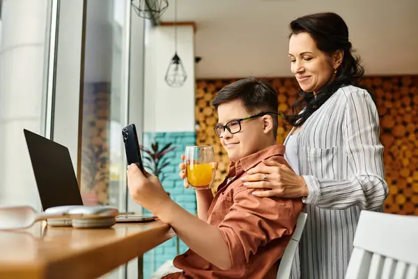 Jolly inclusive preteen boy with Down syndrome sitting in front of laptop and phone next to his mom — Stock Photo