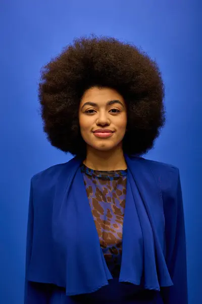 A fashionable African American woman stands confidently in front of a vibrant blue background. — Stock Photo