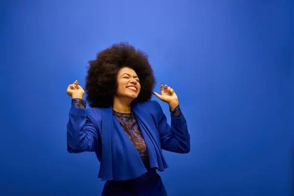 Stylish African American woman with curly hairdosmiling, raising her hands in joy. — Stock Photo