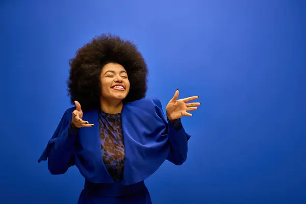 Stylish African American woman with curly hairdoposes against vibrant blue background. — Stock Photo