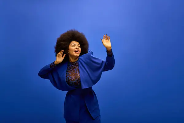 Trendy African American woman in a blue jacket raises her hands gracefully. — Stock Photo