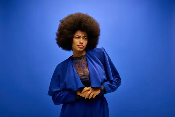 Mujer afroamericana de moda con el pelo rizado posa delante de fondo azul vivo. - foto de stock