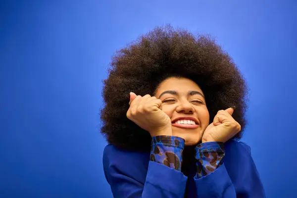 Una mujer afroamericana con estilo con cabello rizado millas y sostiene sus manos en frente de su cara en una pose alegre. - foto de stock