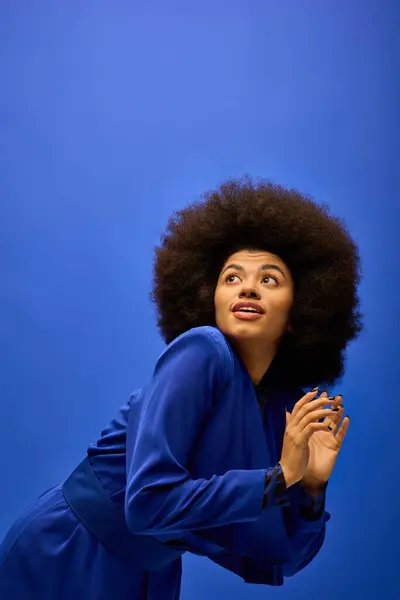 Fashionable African American woman in trendy attire and afro hairstyle, posing confidently in front of a bright blue backdrop. — Stock Photo