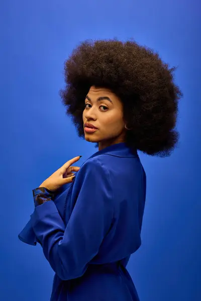 Mujer afroamericana de moda con el pelo rizado se para con confianza delante de fondo azul brillante. — Stock Photo