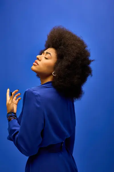 A fashionable African American woman with curly hairdohairstyle strikes a pose in a blue dress against a colorful backdrop. — Stock Photo