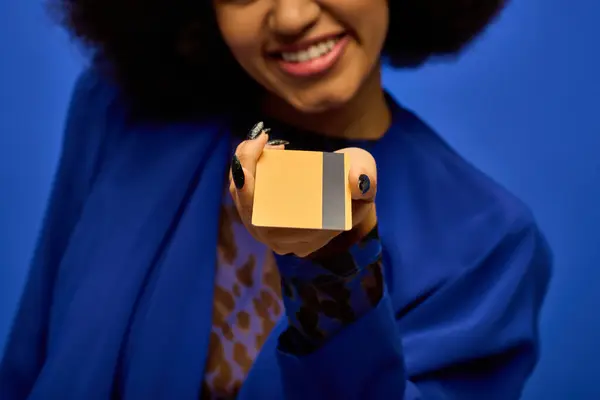 A fashionable African American woman in a blue coat holding up credit card. — Stock Photo
