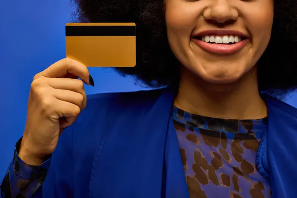 Stylish African American woman in trendy attire holding credit card, smiling. — Stock Photo