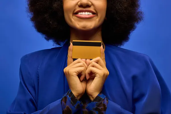 Femme afro-américaine élégante en tenue tendance tenant une carte de crédit à son visage. — Photo de stock