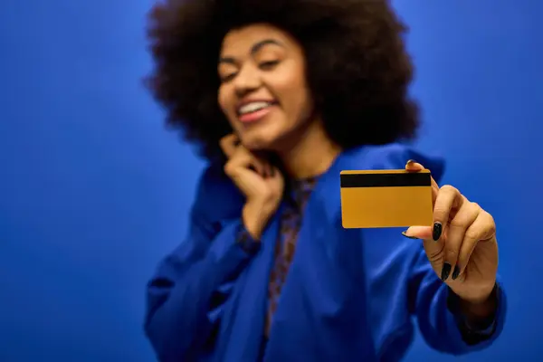 Mujer afroamericana alegre con elegante atuendo sosteniendo una tarjeta de crédito y sonriendo. - foto de stock