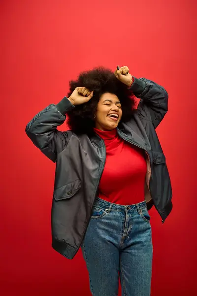A stylish African American woman in a red shirt and black jacket poses against a vibrant backdrop. — Stock Photo