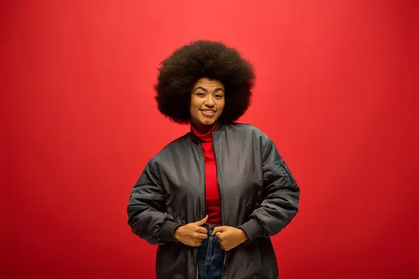 Africano americano mulher com crespos hairdostands confiantemente na frente de um fundo vermelho ousado. — Fotografia de Stock