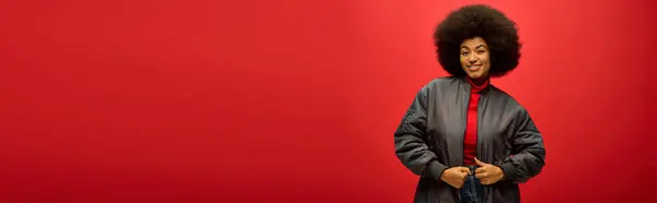 Eine trendige Afroamerikanerin mit lockiger Frisur posiert vor einer roten Wand. — Stockfoto