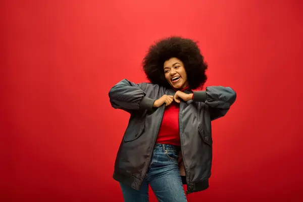 Stylish African American woman with curly hairdohair standing confidently against a striking red background. — Stock Photo
