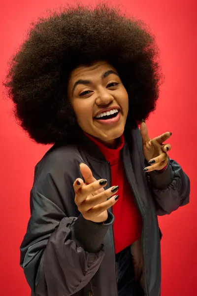 Una mujer afroamericana con estilo con cabello rizado haciendo una cara divertida en un vibrante telón de fondo. - foto de stock