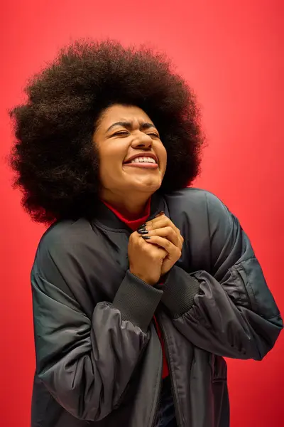 Trendy African American woman with curly hairdohair poses in front of bold red wall. — Stock Photo