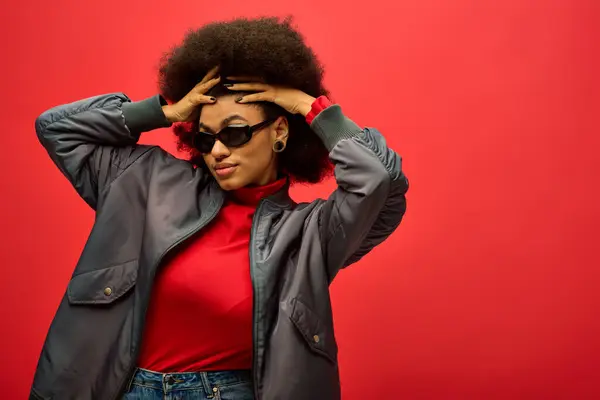 Stylish African American woman poses in trendy red shirt and black jacket against vibrant backdrop. — Stock Photo
